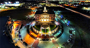 bird's eye view of lighted building at night in the Dallas Texas area, the surrounding area is circular and shows different colored lights in parts of the circle